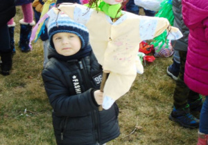 Chłopiec w grantowej kurtce tzyma Marzannę w rękach