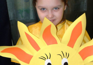 Dziewczynka w żółtej bluzce trzyma w rączkach papierowe słońce