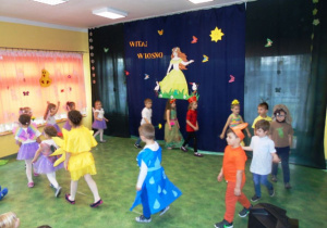 Dzieci w kolorowych strojach tańczą na scenie
