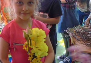 Dziewczynka w różowej bluzce trzyma w rączkach żółte kwiaty