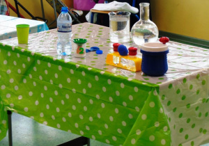 Na biało- zielonym stole stoją przyrządy do robienia eksperymentów