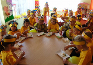 Dzieci ubrane na żółto jedzą przy stole ciasto
