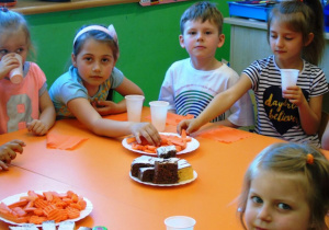 Dzieci siedzą przy stoliku i jedzą marchew i ciasto marchewkowe