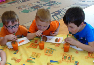 Trzech chłopców pije przy żółtym stoliku sok marchewkowy