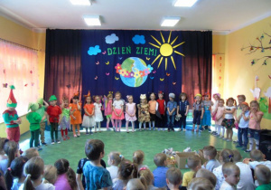 Dzieci stoją w półkole za nimi ciemne tło z napisem Dzień Ziemi