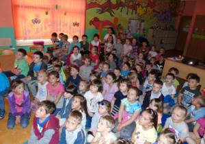 Dzieci siedzą na dywanie wpatrzone w ekranizację filmu