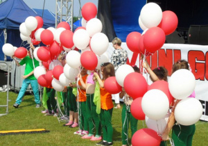 Dzieci z biało- czerwonymi balonami stoją przed sceną