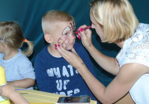 Kobieta maluje twarz chłopca kolorowyni pisakami