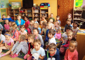 Dzieci siedzą na dywanie w kolorowej sali