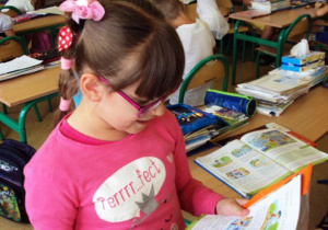 Dziewczynka w różowej bluzce czyta książkę