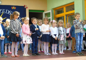 Grupa dzieci stoi na scenie a chłopiec mówi przez mikrofon wiersz