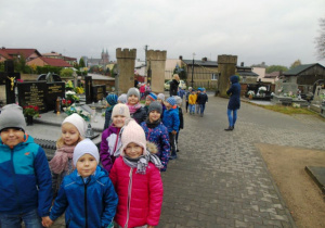 Dzieci idą z opiekunami przez cmentarz w Gorzkowicach