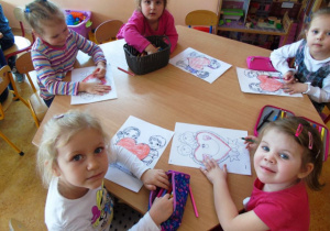 Pięć dziewczynek z grupy Motylki siedzi przy stoliku i koloruje walentynkowe malowanki