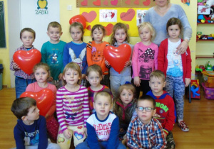 Zdjęcie grupowe dzieci z oddziału przedszkolnego Żabki wraz z wychowawcą, czworo dzieci trzyma balony w kształcie serca
